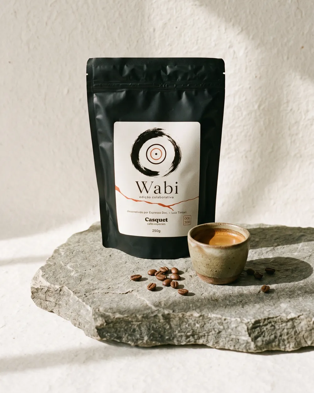 Pacote preto do café Wabi sobre pedra, ao lado de uma xícara de espresso